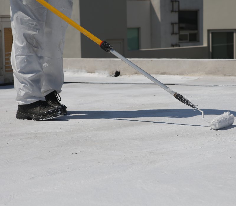 Professional applying roof coating with a roller brush to protect and extend the lifespan of a commercial flat roof.