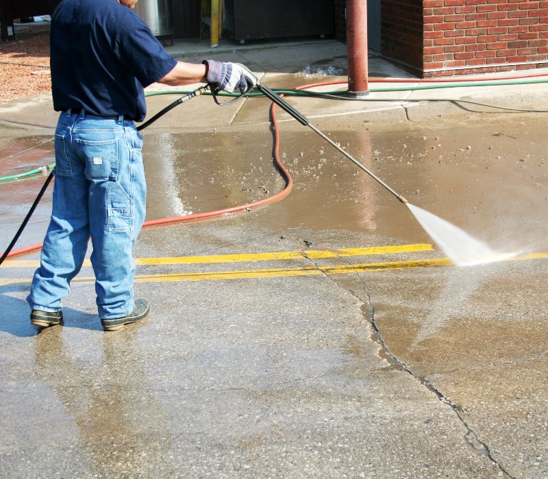 A professional power washing specialist performs commercial concrete cleaning on a parking lot.
